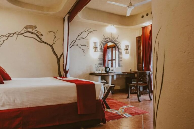 Une chambre au mur peint d'un arbre et de deux singes, avec un bureau sous un miroir en soleil