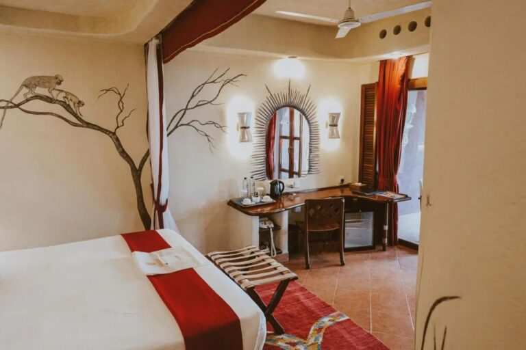 Une chambre avec un porte-bagages, un bureau, une bouilloire et un petit réfrigérateur, sous un ventilateur de plafond