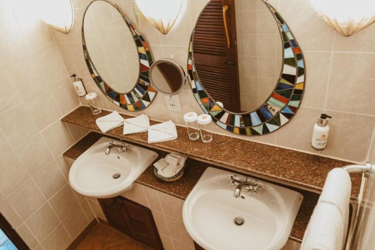 Une salle de bains à deux lavabos, avec un miroir grossissant entre deux miroirs en mosaïque