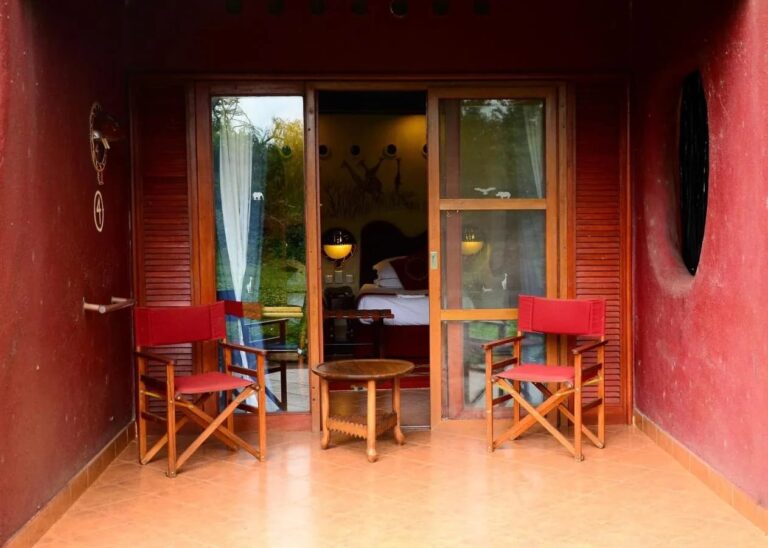 La terrasse d'une chambre entre deux murs rouges, avec deux fauteuils pliants rouges et une table ronde