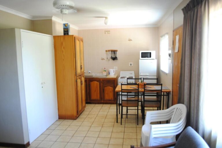 La pièce de vie d'un chalet, avec un coin cuisine, une table à manger, une armoire en bois et une chaise blanche