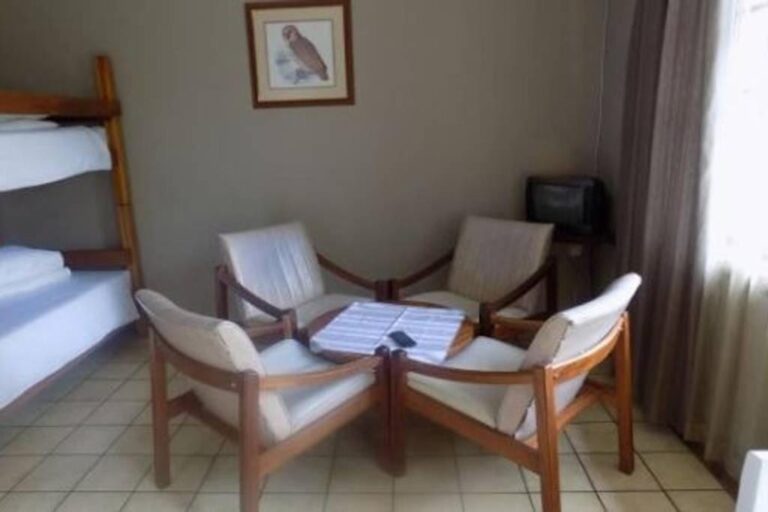 Quatre fauteuils à coussins blancs autour d'une table basse, à côté d'un lit superposé, sous un tableau de chouette