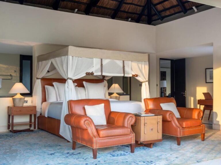 Une chambre au lit à baldaquin, avec deux fauteuils en cuir orange