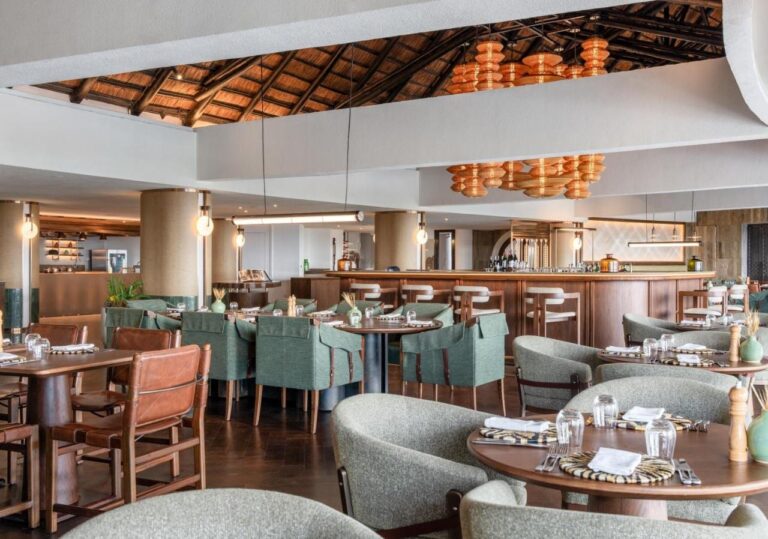 Un restaurant aux fauteuils verts, devant un long bar, sous des suspensions orange