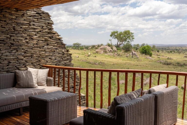 Une terrasse aux fauteuils tressés, entre un mur de pierres empilées et la savane semée de rochers