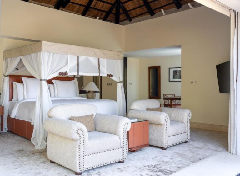 Une chambre au lit à baldaquin, avec deux fauteuils blancs capitonnés