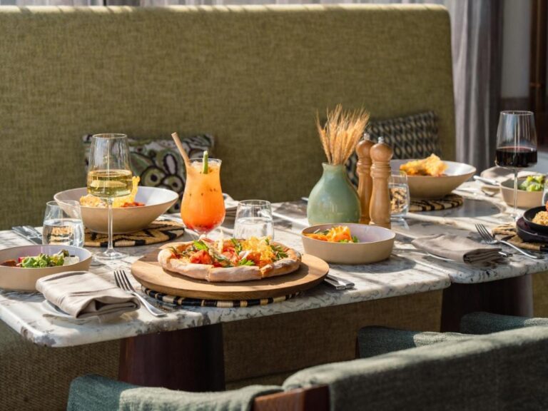 Une pizza, des salades, un cocktail et deux verres de vin sur une table en marbre