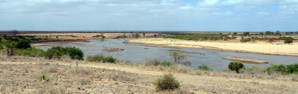 La rivière Galana, large et brune, décrit une courbe entre des bancs de sable clair et des buissons, sous un ciel voilé