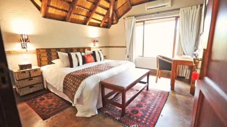 Une chambre sous une charpente de chaume, avec un grand lit, un banc en bois et des tapis rouges