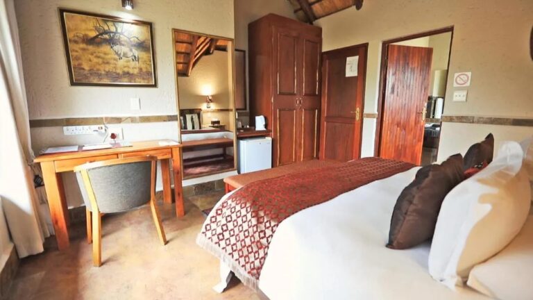Une chambre avec un bureau, une armoire en bois, un petit réfrigérateur et le tableau d'un oryx au mur