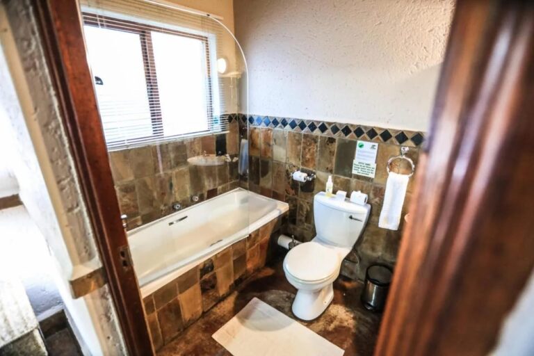 Une salle de bains avec baignoire et toilettes, aux murs carrelés de pierre