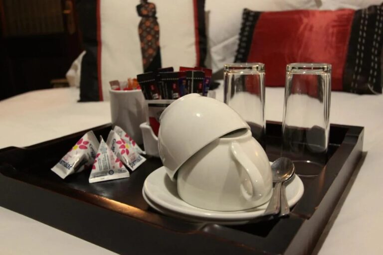 Un plateau avec tasses, verres et sachets de thé et de café, posé sur un lit