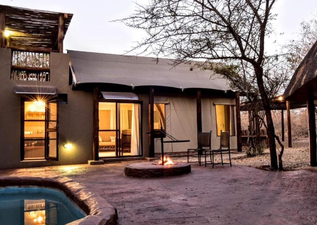 Une tente du Jackalberry Ridge éclairée au crépuscule, avec sa piscine privée, son foyer allumé et deux chaises sur la terrasse