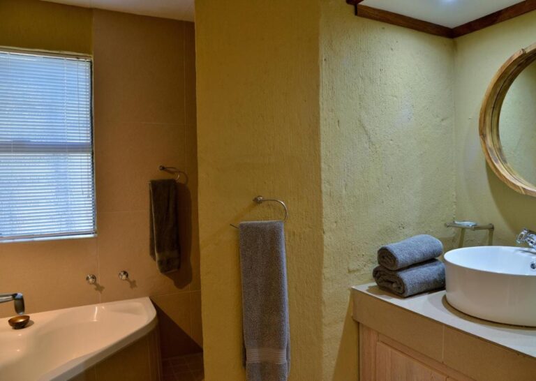 Une salle de bains avec baignoire, vasque ronde posée et miroir rond au cadre en bois