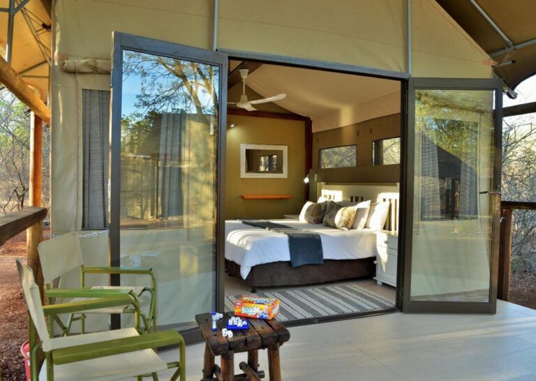 Une tente vue de sa terrasse, portes vitrées ouvertes sur le lit, avec des fauteuils verts devant
