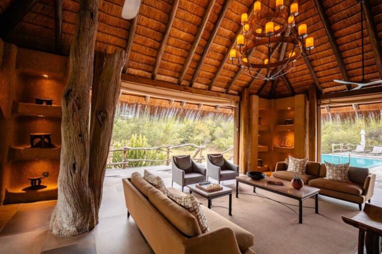 Le salon du Kapama River Lodge sous un haut toit de chaume, ouvert sur une piscine et la brousse