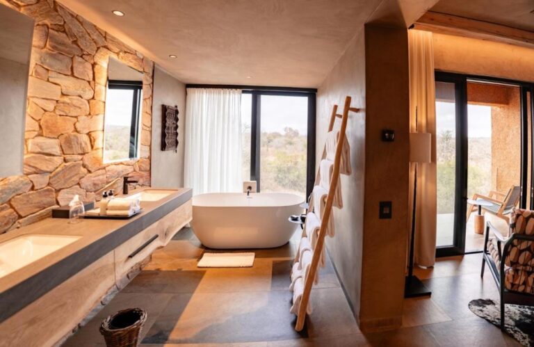 La salle de bains d'une suite, avec une baignoire devant la fenêtre et une double vasque contre un mur de pierre