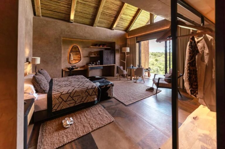 Une suite du Kapama River Lodge sous une charpente de bois et de chaume, avec coin bureau et vue sur les arbres