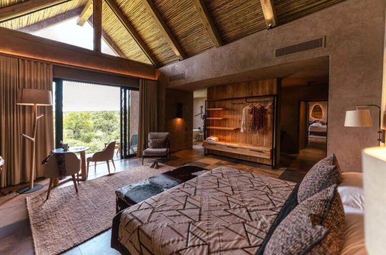 Une suite sous un haut toit de chaume, avec un grand lit, une petite table et une penderie ouverte
