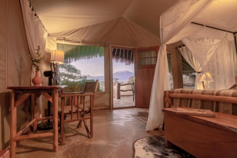L'intérieur d'une tente, avec un bureau, un ventilateur et la porte ouverte sur le Kilimandjaro