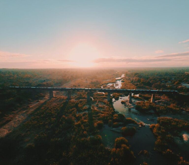 Le train du Kruger Shalati sur le pont de la Selati, vu du ciel, au-dessus de la rivière et de la brousse, le soleil bas sur l'horizon
