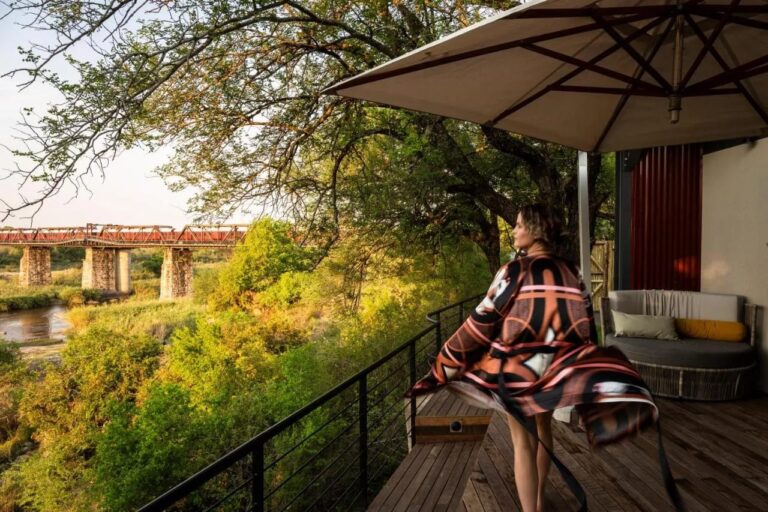 Une femme en peignoir sur une terrasse en bois, sous un parasol, face au pont et à la rivière