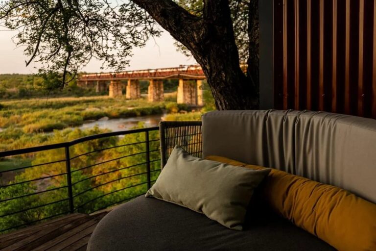 Une banquette arrondie sur une terrasse, sous un grand arbre, face au pont et à la rivière