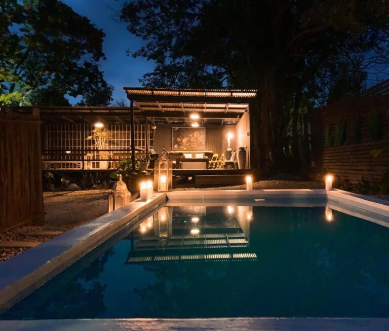 La piscine du Lush à la nuit tombée, éclairée par des bougies, devant une terrasse couverte au toit de tôle