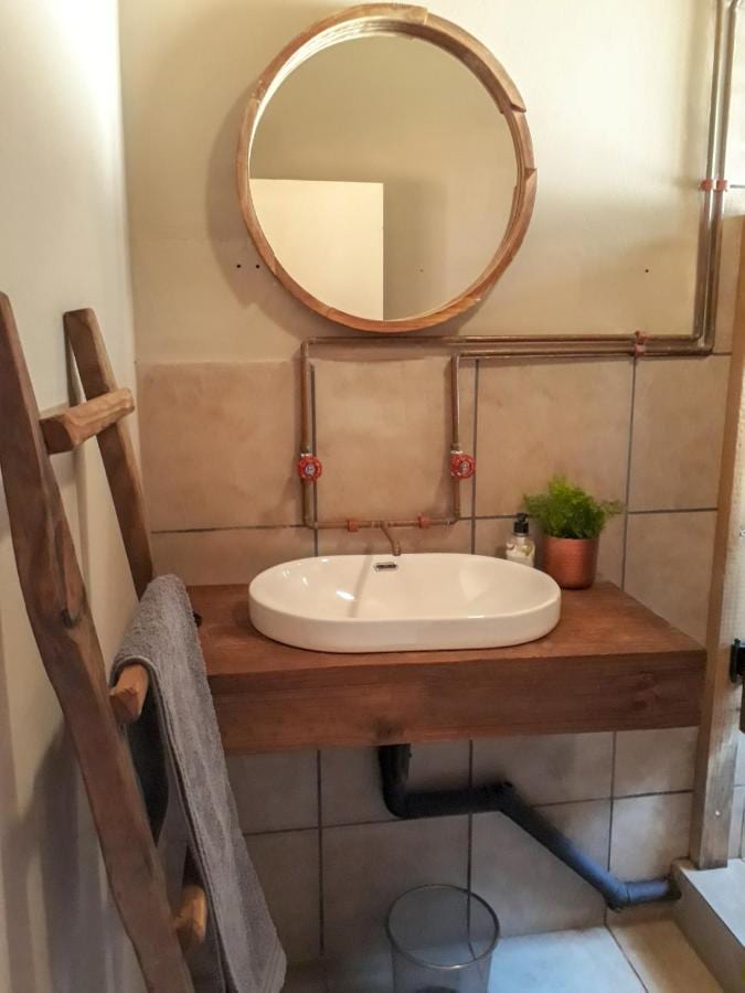 Une vasque blanche posée sur une planche de bois, sous un miroir rond, à côté d'une échelle porte-serviettes