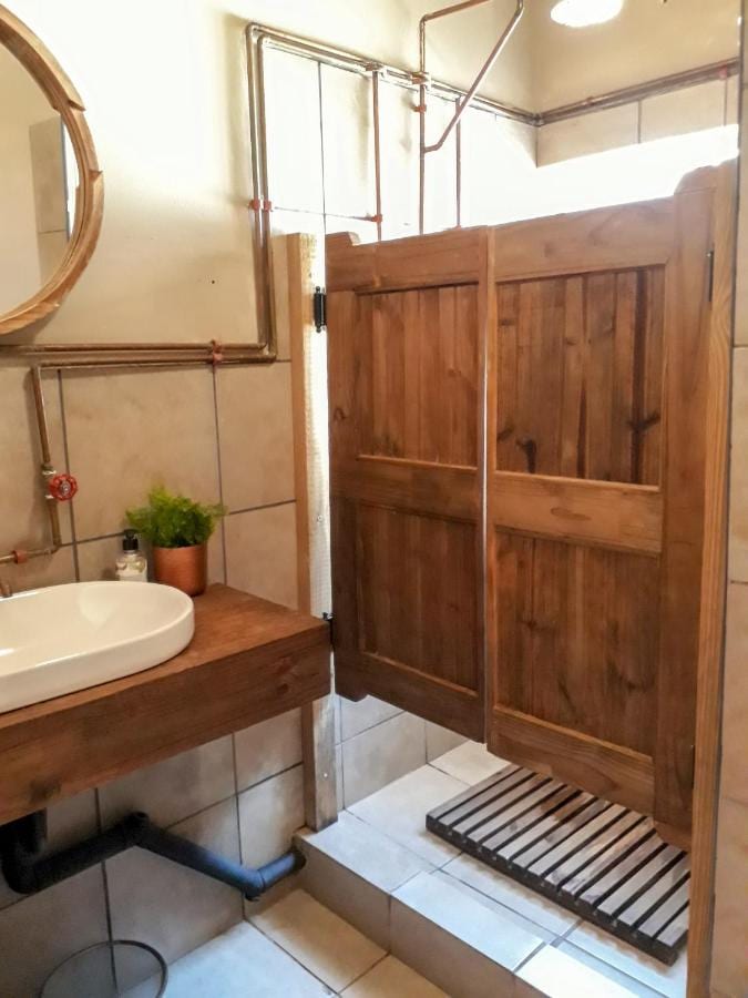 Une douche fermée par des portes battantes en bois, à côté d'une vasque, avec des tuyaux de cuivre apparents