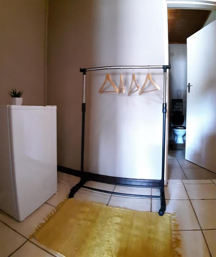 Un petit réfrigérateur et un portant à cintres dans une chambre carrelée, près de la porte ouverte des toilettes