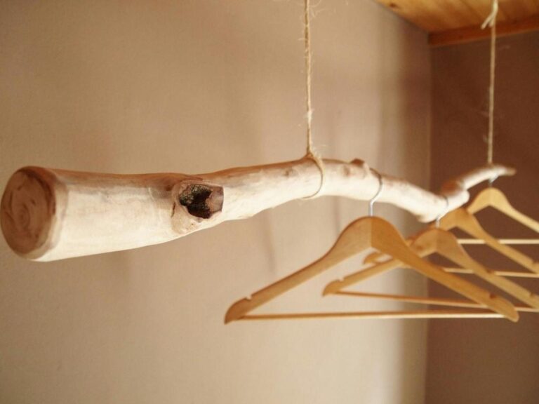 Des cintres en bois accrochés à une branche écorcée, suspendue au plafond par des cordes