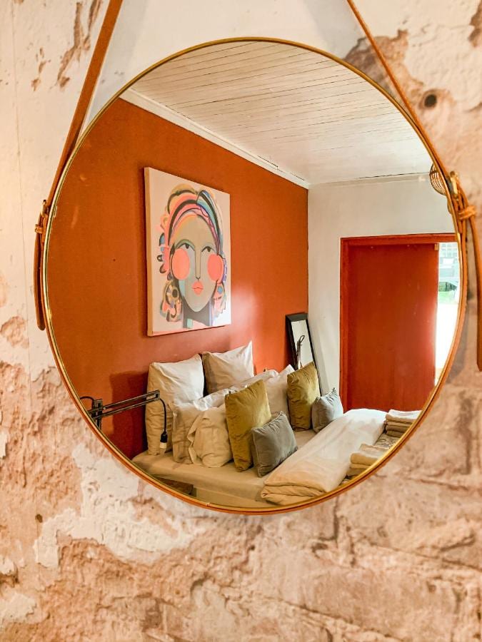 La chambre orange et son grand lit, vus dans un miroir rond suspendu à une sangle, sur un mur à l'enduit écaillé