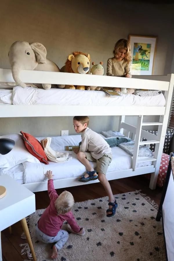 Trois enfants jouent autour d'un lit superposé, avec des peluches d'éléphant et de lion