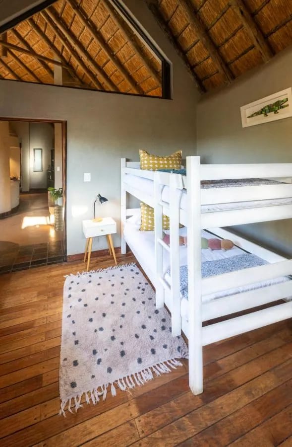 Un lit superposé blanc sous la charpente de chaume, sur un parquet avec un tapis à pois