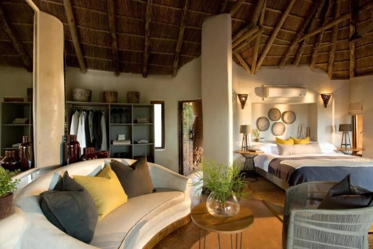 Une suite du Madikwe Safari Lodge avec un canapé blanc arrondi, un grand lit et une penderie ouverte