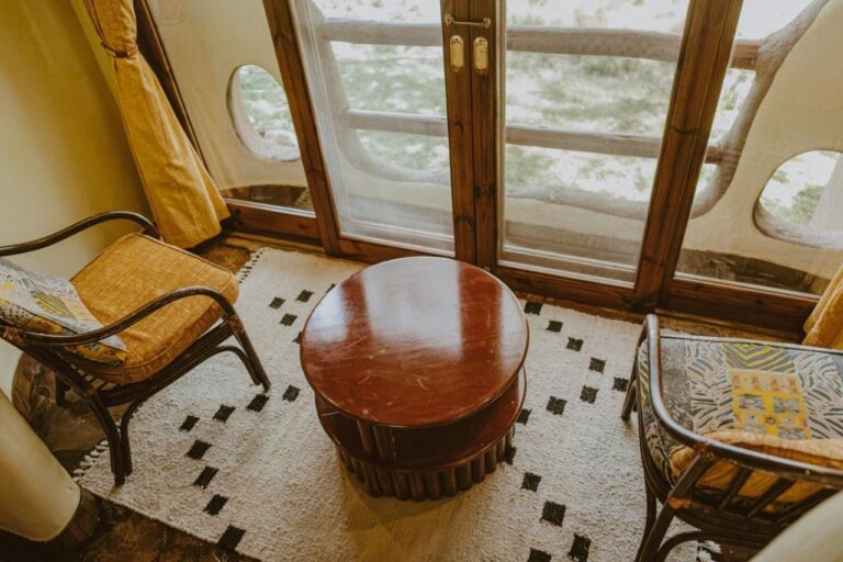 Deux fauteuils et une table ronde devant une porte-fenêtre, avec la savane derrière la balustrade du balcon