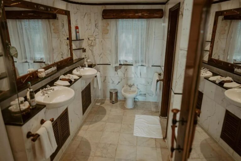 Une salle de bains en marbre blanc, avec deux lavabos, un sèche-cheveux mural et un bidet sous la fenêtre