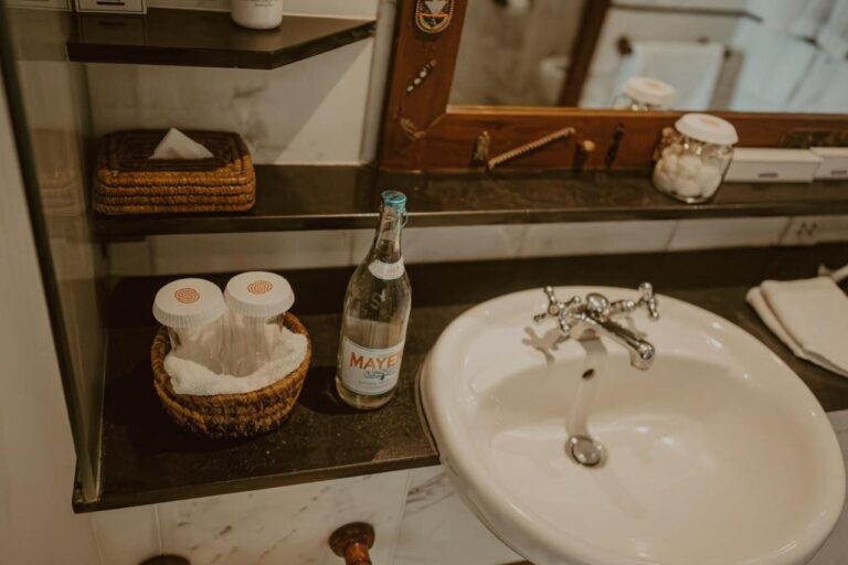 Un lavabo avec une bouteille d'eau, des cotons et une boîte de mouchoirs en osier