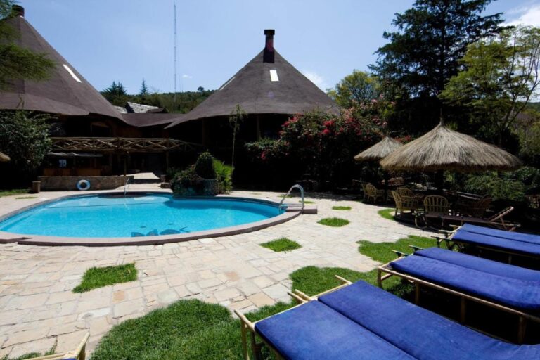 Des transats aux coussins bleus au bord de la piscine, près de parasols en chaume