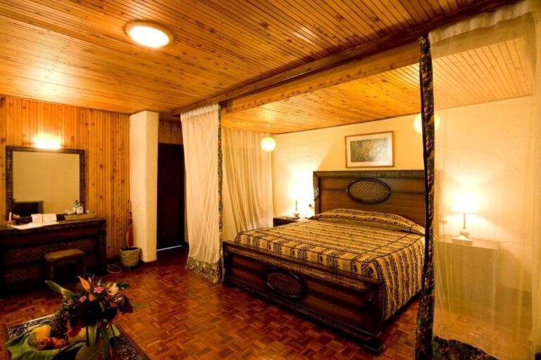 Une chambre au plafond lambrissé, avec un grand lit à baldaquin et une coiffeuse