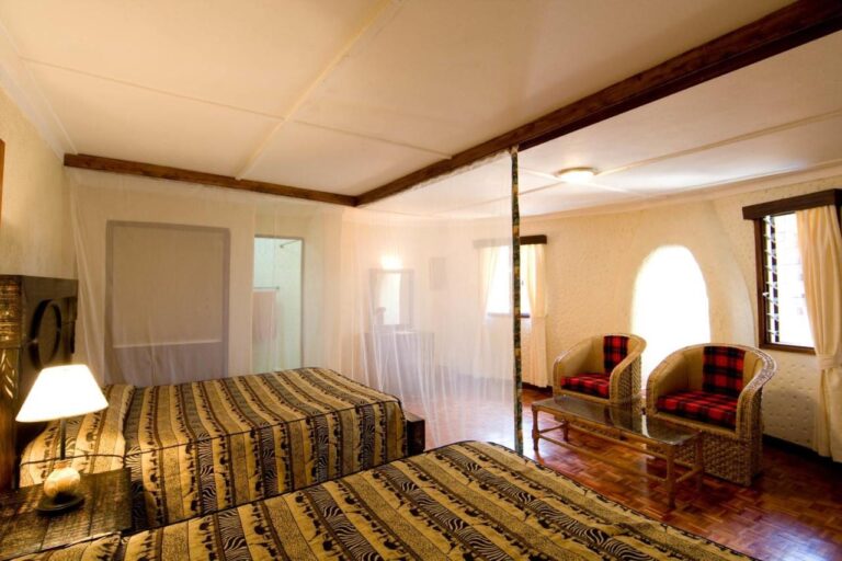 Une chambre à deux lits sous moustiquaire, avec deux fauteuils aux coussins à carreaux rouges