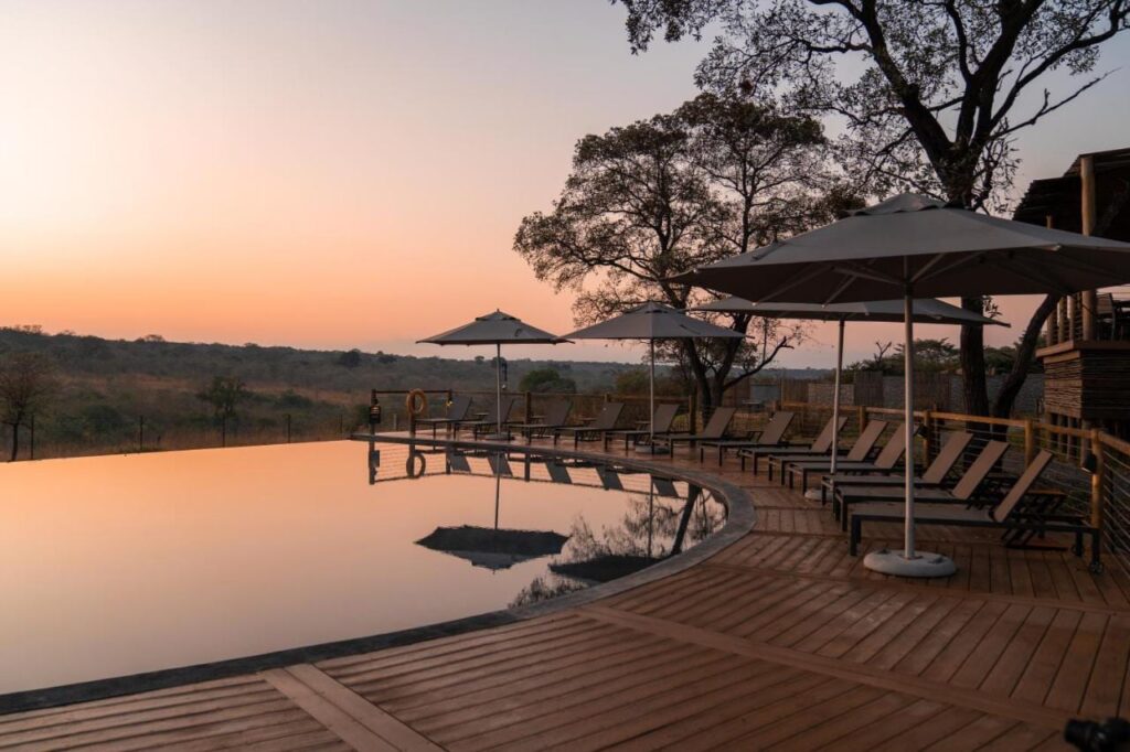 La piscine à débordement du Mdluli Safari Lodge sous un ciel orangé, bordée de transats et de parasols