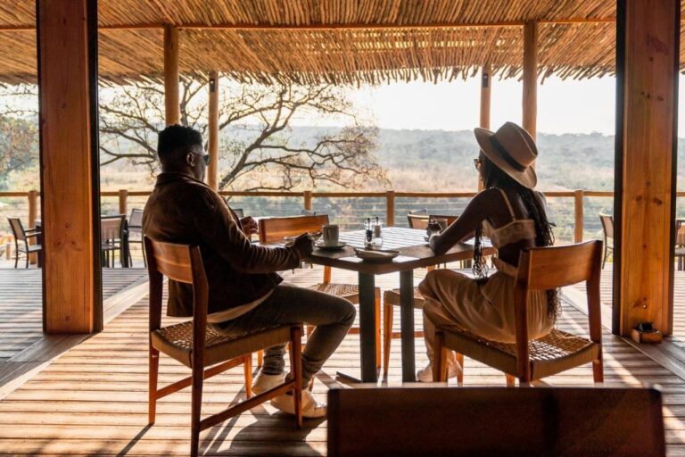 Un couple à table sur la terrasse couverte du lodge, face à la brousse