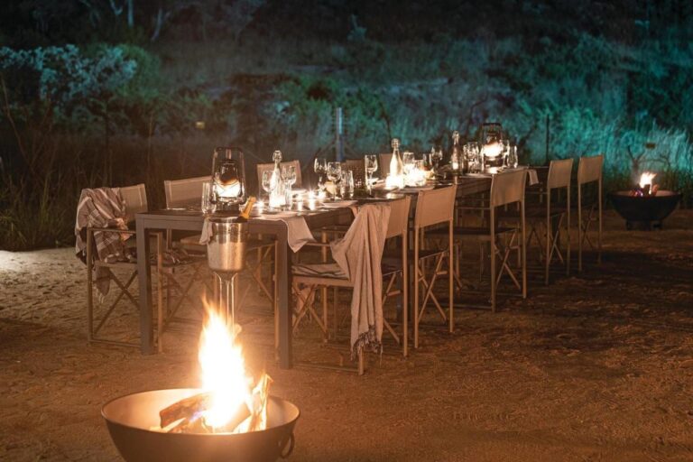Une longue table dressée pour le dîner en plein air, entre lanternes et feux dans des braseros