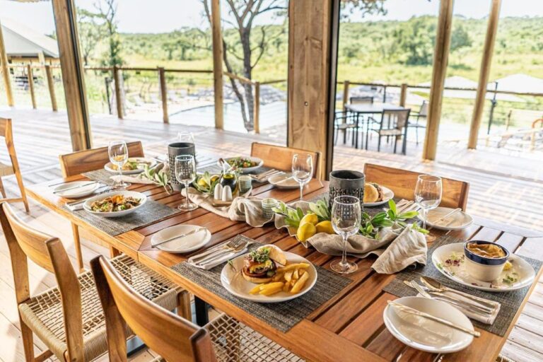 Une table servie au restaurant, ouverte sur la terrasse, la piscine et la brousse