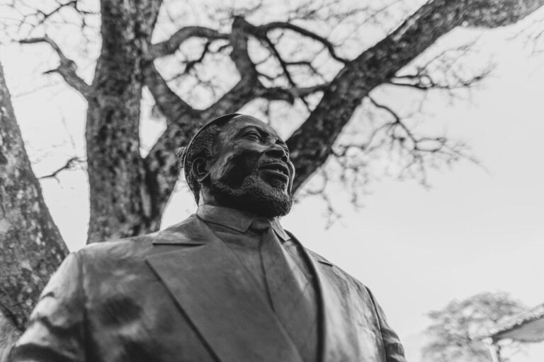 La statue en bronze d'un homme barbu et souriant, en costume, sous un arbre, en noir et blanc