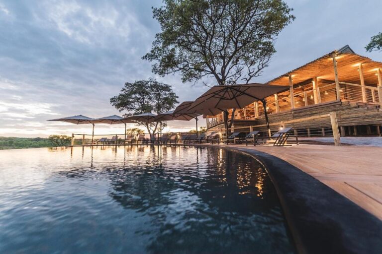 La piscine à débordement du Mdluli Safari Lodge et son bâtiment principal éclairé, sous un ciel nuageux