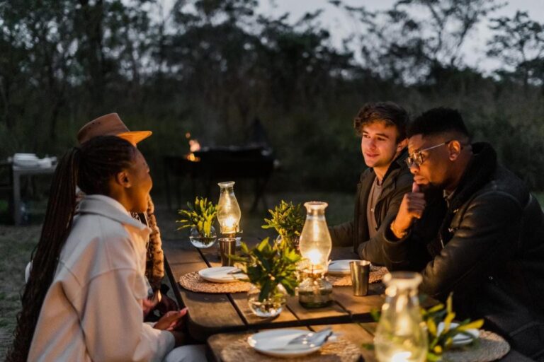 Des convives à une table en plein air, éclairée par des lampes à huile, à la nuit tombante