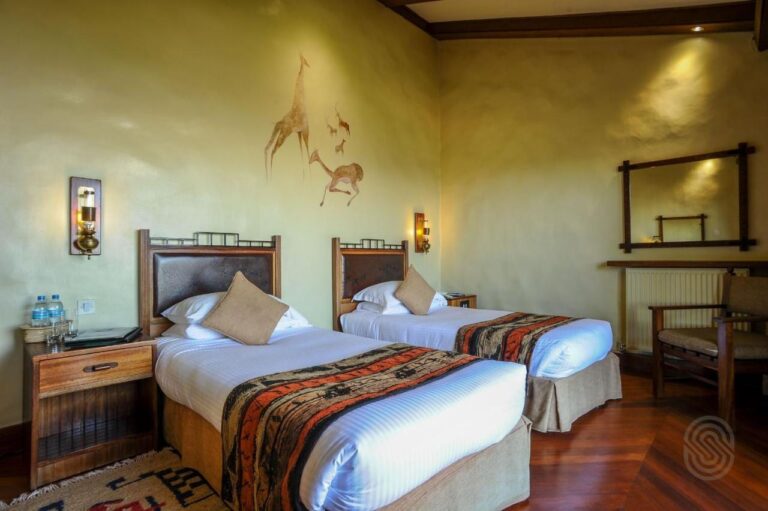 Une chambre à deux lits jumeaux, avec une girafe et des antilopes peintes au mur